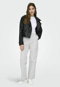 Zwart leren cropped jack, witte t-shirt en gestreepte high-waisted broek. Model draagt witte sneakers; casual outfit met gelaagde details.