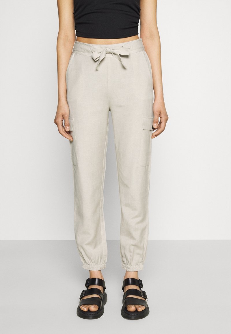 Pantalon jogger en lin beige clair avec une taille élastique et un cordon de serrage, doté de poches cargo latérales et de poignets élastiques aux chevilles.