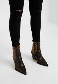 Spetsiga ankelstövlar med ett brunt och tan-snake skin-mönster, blockklack och siddragkedja. Bärs med svarta ripped jeans.