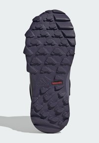 Adidas Traxion shoe sole, featuring a rugged black rubber material, hexagonal and triangular tread patterns for traction, with a red logo accent.