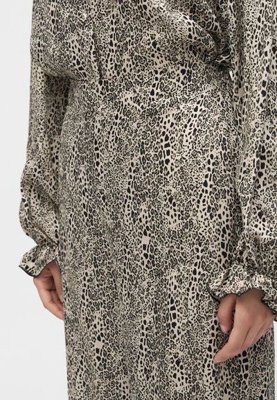 Gros plan d'une personne portant un chemisier beige et noir à imprimé léopard et un pantalon assorti avec poignets froncés et taille haute.