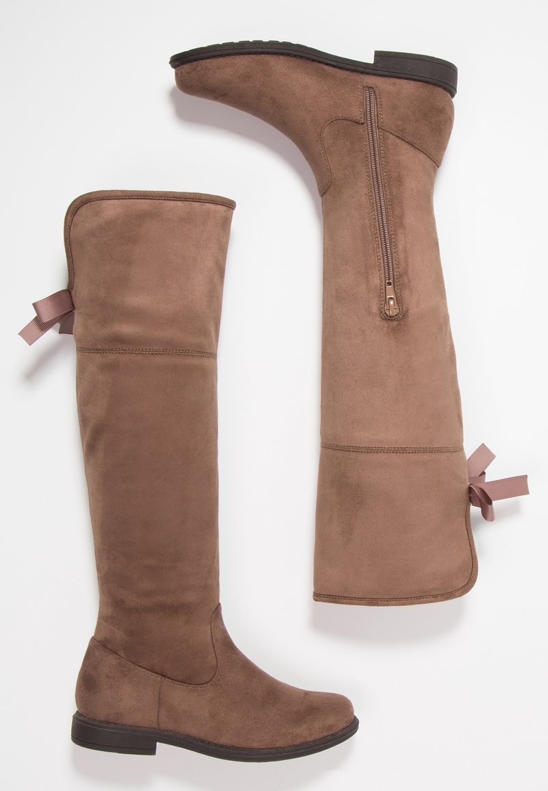 Bottes montantes en daim marron avec semelles plates noires, fermeture éclair latérale et détail ruban rose à l'arrière près du haut.