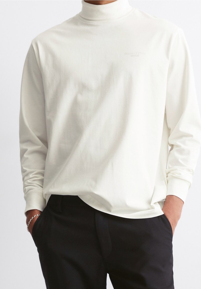 Camiseta de cuello alto de manga larga en color crema, confeccionada en una tela suave, con un sutil estampado del logo en el pecho y un corte relajado.