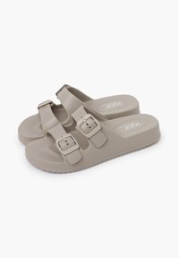 Beige sandaler lavet af struktureret syntetisk materiale, med to justerbare stropper med rektangulære spænder og en behagelig forhøjet sål.