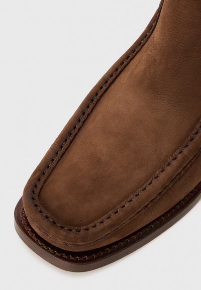 Bruna mocka ankelboots med rund tå, dekorativ sömnad och en slät yta. Sula med en kontrasterande brun kant.
