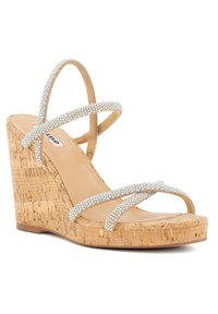 Wedge sandaal met een kurken platform, voorzien van kruisende zilveren bandaccenten versierd met rhinestones op een tan basis.
