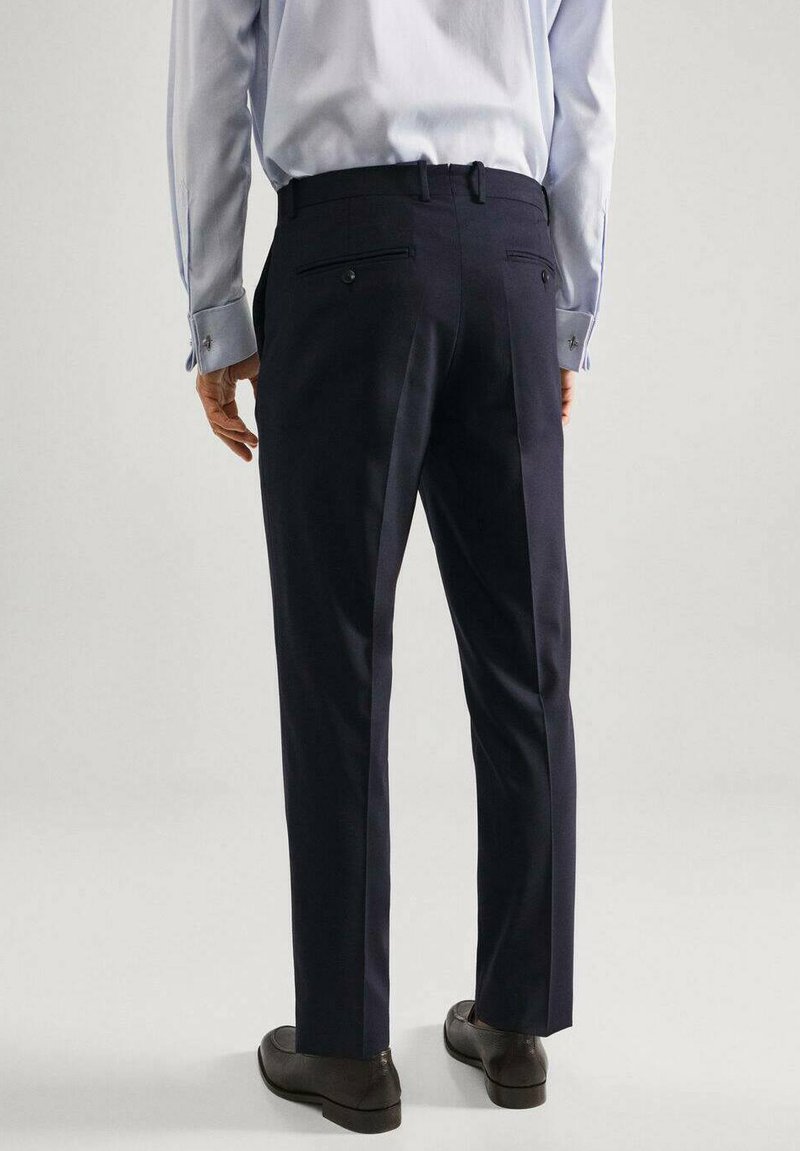 Pantalons bleu marine foncé en tissu à texture lisse, dotés de deux poches arrière et d'un design à jambes droites. Portés avec une chemise bleue claire.