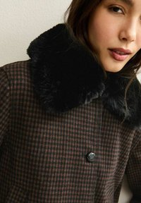 Bruin en zwart geblokt jasje met een zwarte nepbont kraag, voorzien van een enkele zwarte knoop en een gladde, gestructureerde stof.