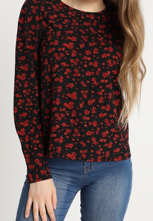 Haut noir à manches longues avec un motif floral rouge, col rond et coupe décontractée. Associé à un jean bleu pour un look casual.