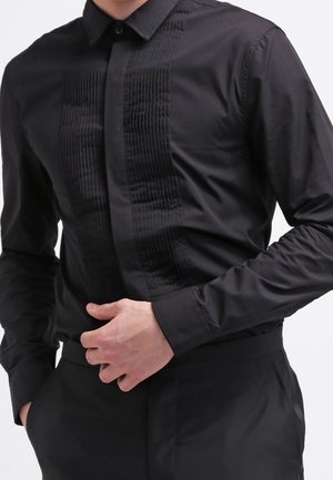 Zwarte lang mouwen shirt met een gestructureerde verticale streep aan de voorzijde, met een knoopsluiting bij de kraag en een gladde stof. Getailleerde pasvorm.