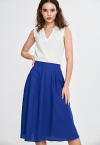 Niebieska, plisowana midi spódnica wykonana z lekkiego materiału, połączona z białym topem bez rękawów z dekoltem w serek. Gładka tekstura i swobodny fason.