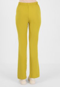 Elastyczne, musztardowo-żółte spodnie dzwony z elastyczną talią. Gładka tekstura bez widocznych wzorów czy elementów metalowych.