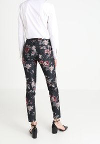 Jean imprimé floral noir, avec une combinaison de fleurs roses et blanches, coupe slim, poches arrière et une texture de tissu lisse.