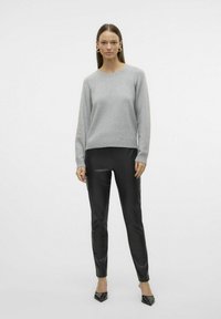 Pull en tricot gris avec un col rond, associé à un pantalon en cuir synthétique noir et des escarpins noirs à bouts pointus. Texture lisse et design ajusté.