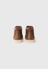 Bottines en cuir marron avec une finition texturée, bout rond, semelle en caoutchouc crème et col rembourré doux. Présente des accents contrastants sur le talon.