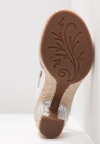 Brązowa gumowa podeszwa z kwiatowym wzorem, pleciony akcent z jutowego materiału oraz przezroczysty, teksturowany obcas. Górna część ma biały wzór paska.