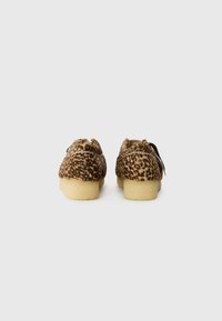 Sko med leopardmønster, myk tekstur, rund design og lyse gummisåler. Baksidevisning som viser sømmer og detaljer.