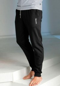 Zwarte sweatpants met taps toelopende pijpen, elastische tailleband, trekkoord en een witte "Bench." logo op de zijkant. Gemaakt van zachte stof, geschikt voor casual kleding.