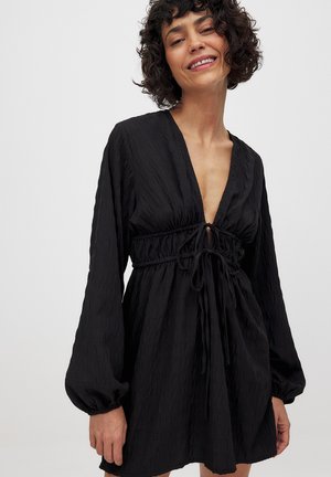 Schwarzes Kleid mit tiefem V-Ausschnitt, langen Puffärmeln mit elastischen Bündchen und einem taillierten Kordelzug. Strukturierter Stoff mit einem dezenten Muster.