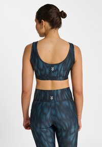 Komplet biustonosza sportowego i legginsów w ciemnoniebieskim kolorze z abstrakcyjnymi wzorami. Materiał wydaje się elastyczny; charakteryzuje się gładkim wykończeniem i subtelnymi detalami z logo.