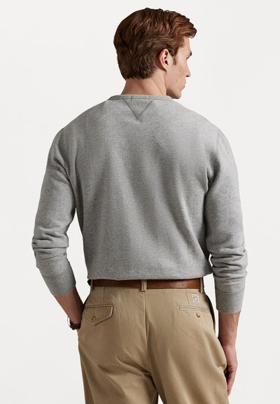 Sweatshirt cinza com decote redondo e mangas longas, apresentando punhos canelados. Usado com calças caqui e um cinto castanho.