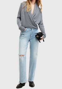 Szary sweter z długimi rękawami, połączony z jasnoniebieskimi spodniami typu straight-leg z przetarciami oraz czarnymi botkami za kostkę. Czarna torba z złotymi akcentami.