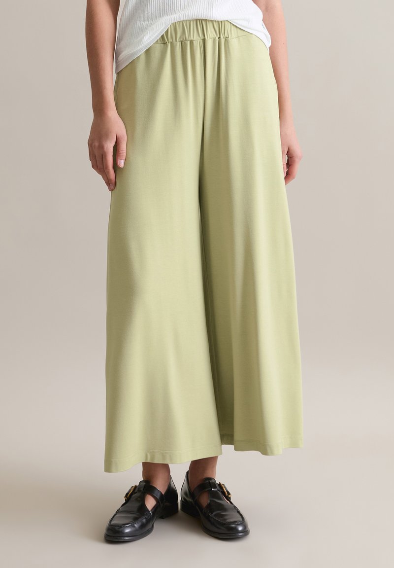 Hellgrüne, weite Hose aus einem weichen Material mit elastischem Bund, kombiniert mit schwarzen Schuhen mit einer dekorativen Schnalle.