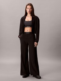 Jaqueta preta curta, sutiã desportivo combinando com logo e calças largas; textura suave, design minimalista e silhueta elegante.