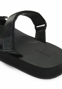 Svart sandaler med justerbara tygremmar, platt gummisula, strukturerad sula och upphöjd logotypdetalj på remmen.