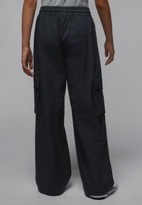Pantaloni cargo neri con design a gamba larga. Realizzati in materiale leggero con due tasche laterali e vita elastica.