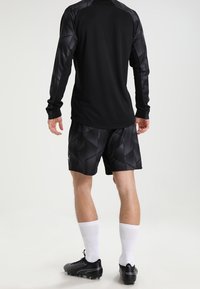 Svart långärmad sporttröja med mönstrade ärmar, ihop med svarta shorts med geometriskt mönster. Vita strumpor och svarta sportskor fulländar looken.