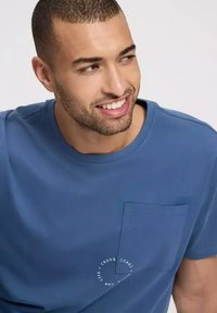 Niebieska bawełniana koszulka z kieszonką na piersi i okrągłym detalem logo. Gładka faktura z klasycznym okrągłym dekoltem.