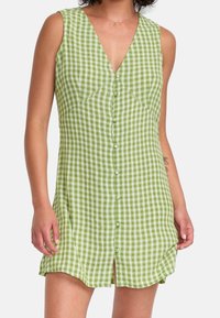 Robe en vichy vert avec un col en V, sans manches et boutons sur le devant. Caractérisée par une coupe décontractée et des fentes sur les côtés pour la mobilité. Tissu en coton.