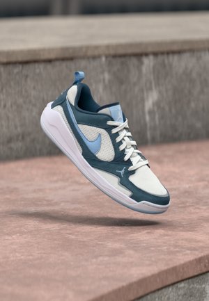 Blue and white Nike Air Jordan sneaker floating above a concrete surface with a blurred stone background.