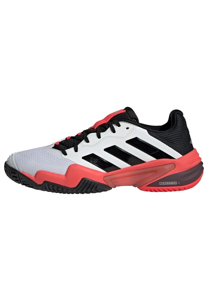 Sportschuh mit einem weißen Mesh-Obermaterial, schwarzen Akzenten und einer roten Zwischensohle. Verfügt über drei schwarze Streifen und eine strukturiert gummierte Laufsohle.
