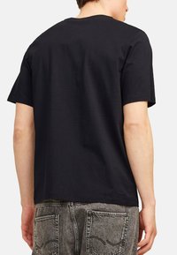 Schwarzes T-Shirt mit kurzen Ärmeln, aus Baumwolle gefertigt, mit klassischem Rundhalsausschnitt und glatter Textur, getragen mit grauen Jeans.