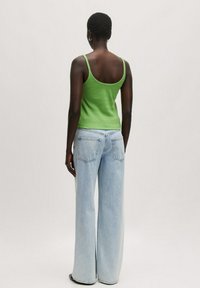 Grünes geripptes Tank-Top kombiniert mit weitgeschnittenen hellblauen Jeans, die über Gesäßtaschen und eine lockere Passform verfügen. Minimalistisches Design mit dünnen Trägern.