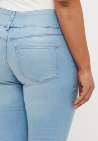 Light blue denim jeans with a fitted waist, mid-rise design, and a single back pocket. The fabric has a smooth, slightly faded texture.