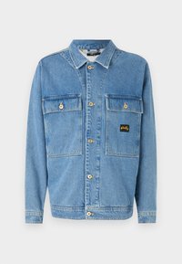 Light blue denim jacket featuring a button-up front, two chest pockets with flaps, and a small logo patch. Classic collar and long sleeves.
