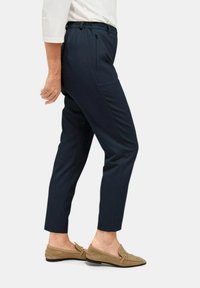 Donkerblauwe broek met een tapered ontwerp, voorzien van een elastische tailleband en zijzakken. Glad materiaal met een gepolijste afwerking.