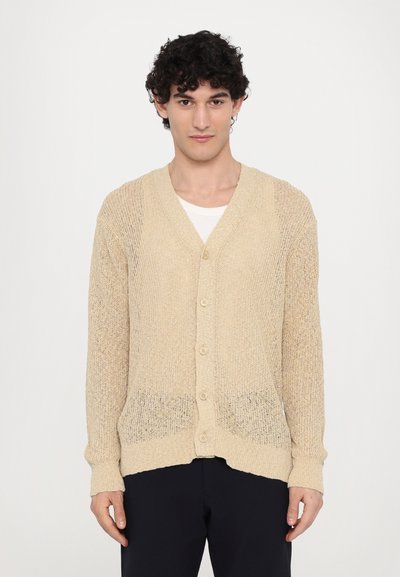 Beige pletený kardigan s výstřihem do V, předními knoflíky a žebrovanými manžetami. Textura je volně pletená, což poskytuje lehký vzhled.