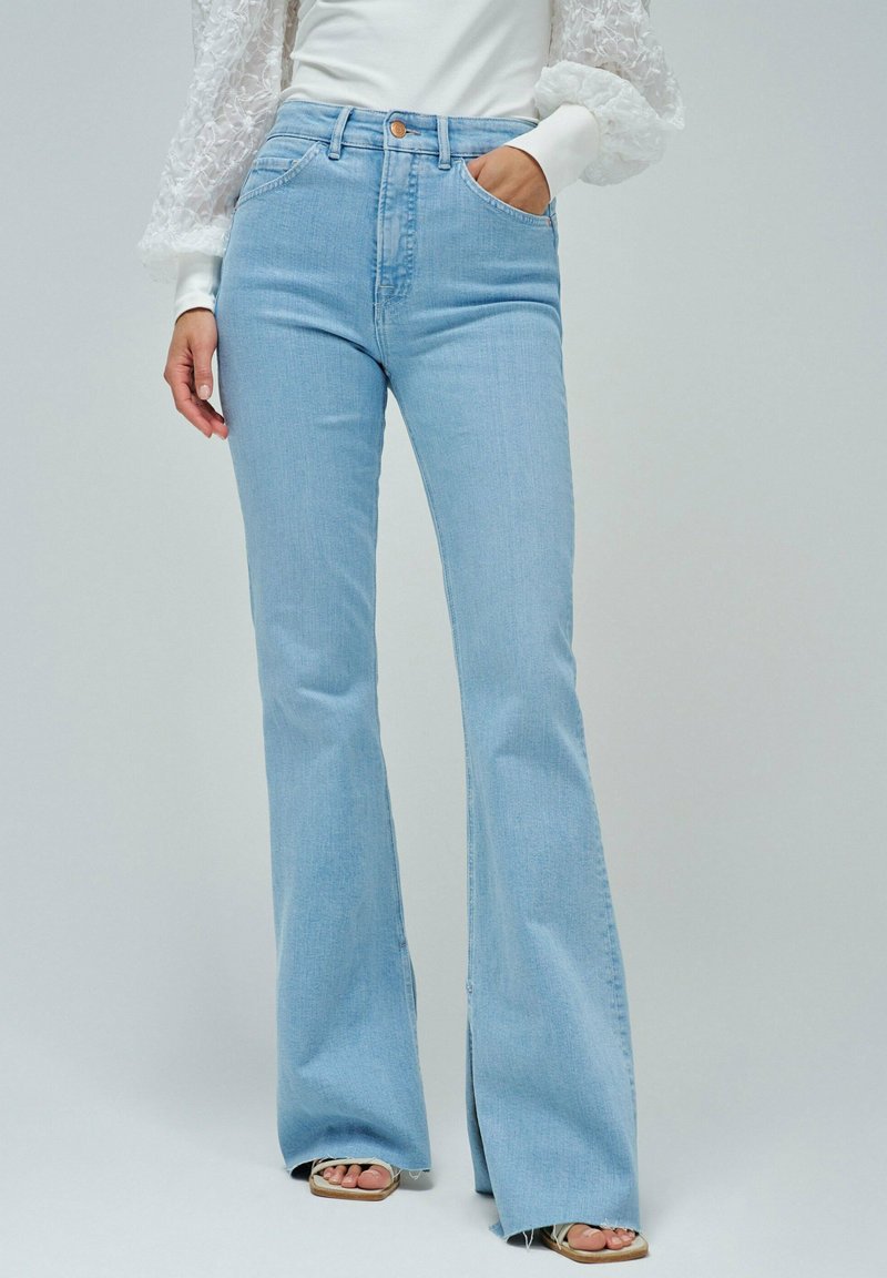 Jeans acampanados de color azul claro con cintura alta, que cuentan con bolsillos frontales, cierre de botón y dobladillos divididos en los tobillos. Material de mezcla de algodón.