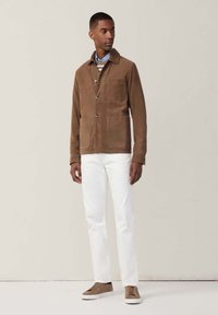 Giubbotto in suede marrone con quattro tasche, camicia blu e maglione a righe sotto, abbinato a pantaloni bianchi e sneakers marroni.