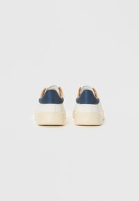 Două adidași cu un corp alb, cu toc din albastru marin și accente bej. Material texturat și design minimalist; talpă din cauciuc.