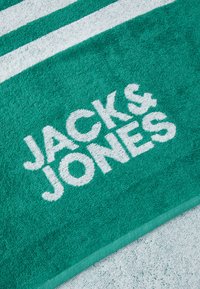 Serviette turquoise avec des rayures blanches et le logo "JACK & JONES" en texture douce et absorbante ; bordée d'un bord turquoise uni.