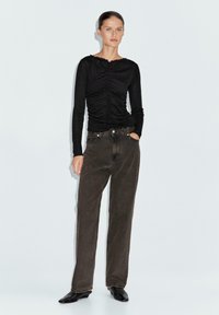 Maglietta nera a maniche lunghe con texture arricciata sul davanti, abbinata a jeans marroni a vita alta e scarpe nere a punta.