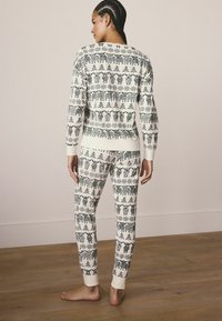 Strick-Pyjama-Set in Creme mit grünen Baum- und Bärenmotiven. Verfügt über lange Ärmel, gerippte Bündchen und knöchellange Hosen. Weicher Stoff.