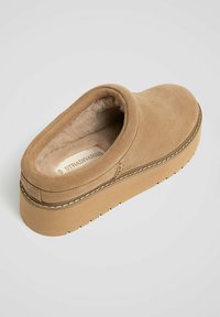 Tan suede slip-on shoe with a soft fur lining, featuring a thick beige sole and visible stitching along the edge. Minimalistic design.