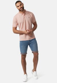 Polo rose clair avec détail de col blanc, associé à un short en denim roulé et des baskets blanches ; coupe décontractée, tissu texturé.