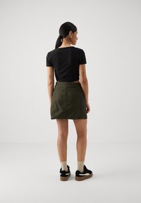 Svart avkortet topp kombinert med et grønt skjørt med teksturert finish, baklås og sidelommer, supplert med svarte sneakers.